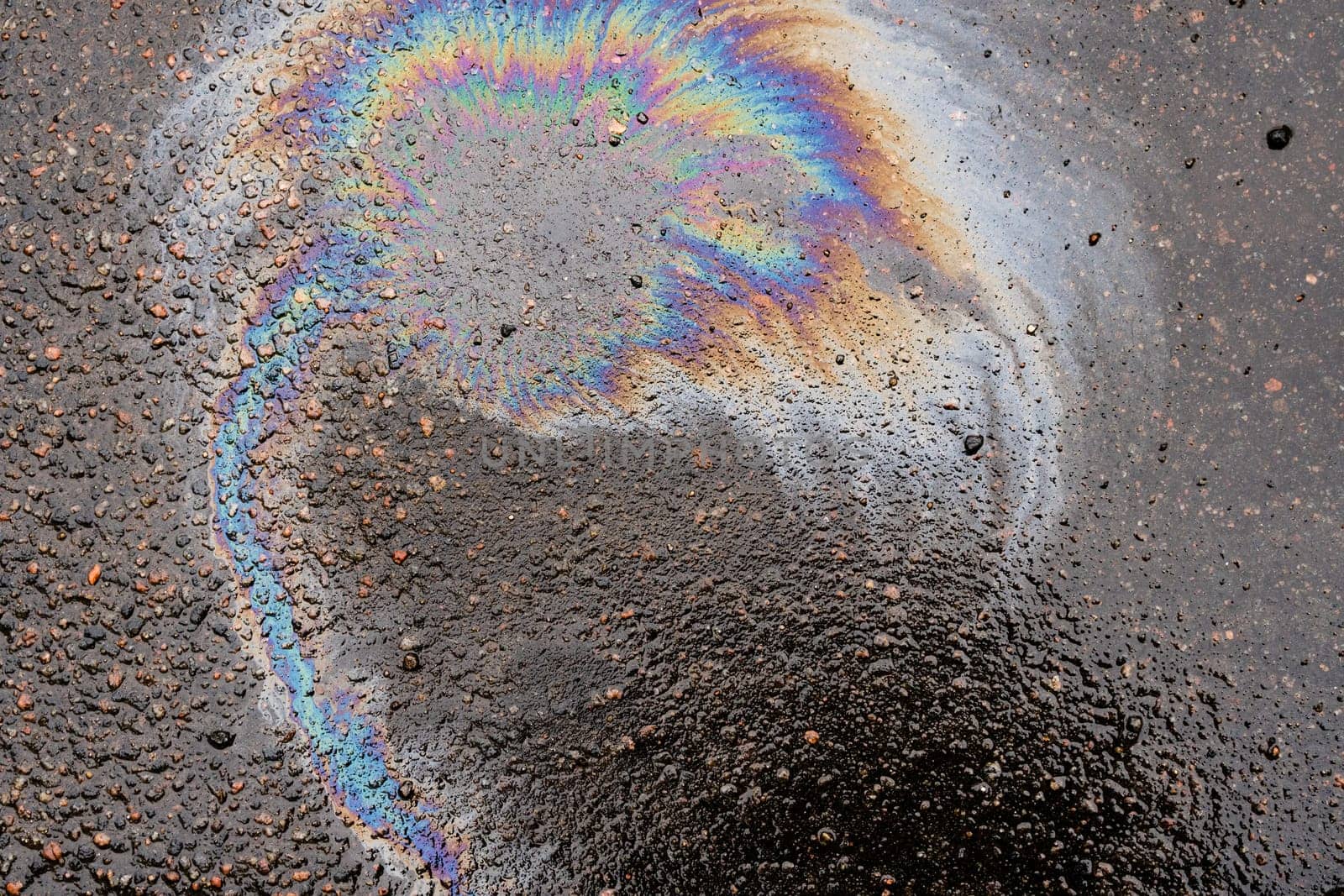 Oil stains from leaks in the car engine. Oil after rain makes spots with rainbow reflections refractive sun spectrum. Beautiful color mosaic, abstraction, ecology