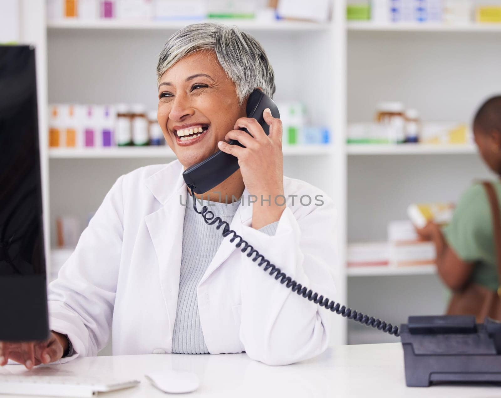 Pharmacist, conversation and customer service with telephone for call with computer. Female chemist, working and online for communication for job with tech for help with medicine at drugstore