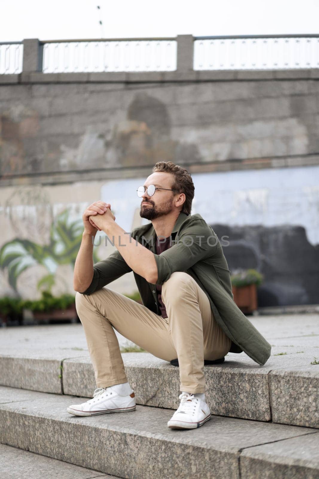 Dreamer, man seated on outdoor stairs, lost in thoughts and dreaming about plans for future. With serene and peaceful expression, he contemplates aspirations and envisions goals. . High quality photo