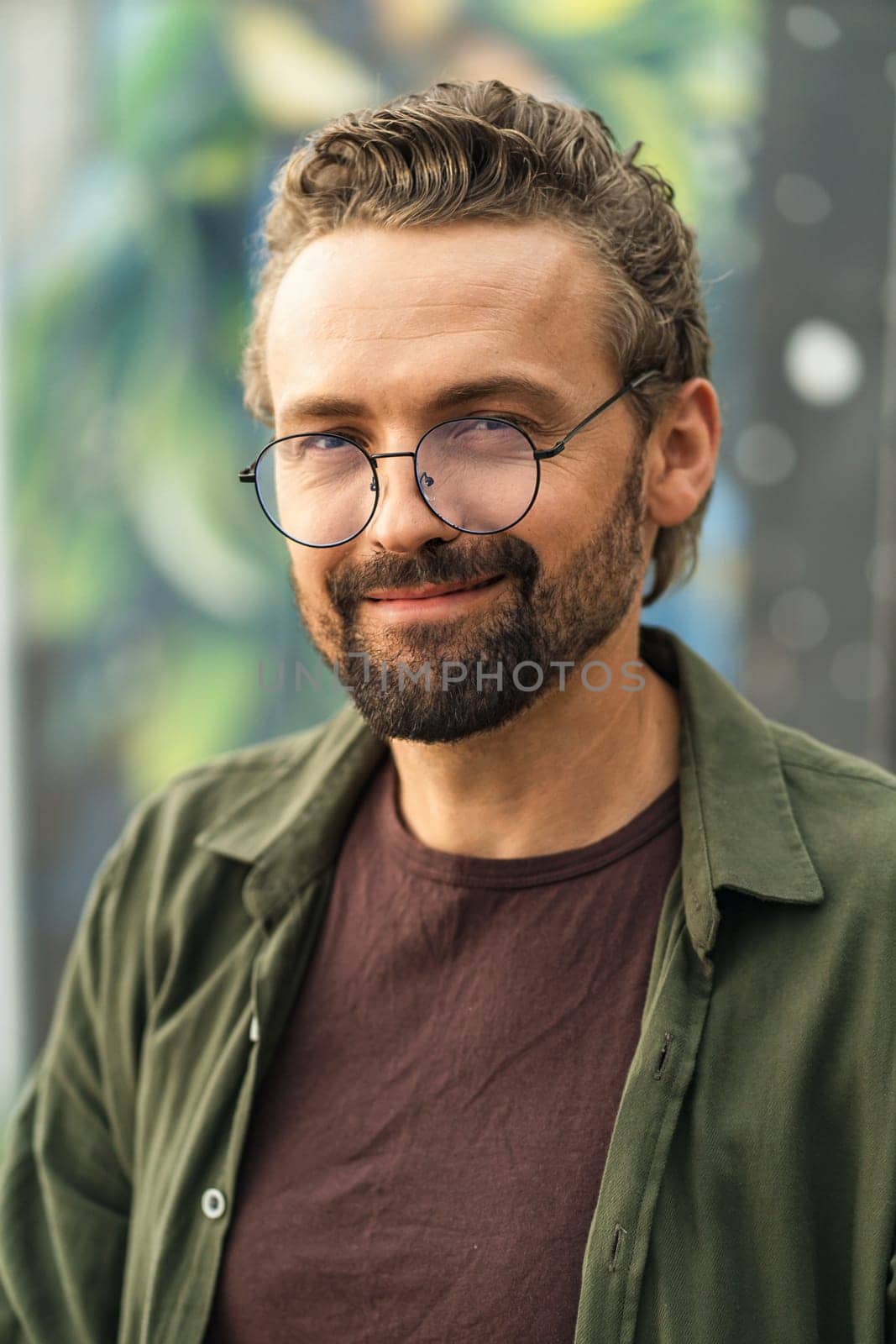 Handsome individual wearing glasses, situated outdoors against a graffiti-covered background. With a stylish and confident appearance, the subject exudes a modern and trendy vibe. by LipikStockMedia