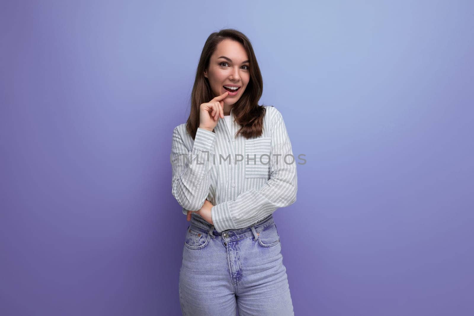 positive pretty young brunet female adult in striped shirt and jeans isolated on plain background.