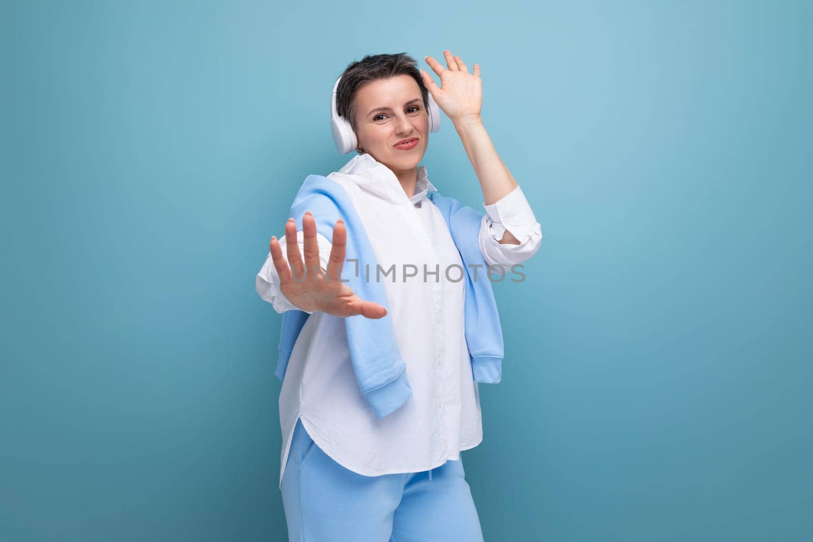 dude young woman with a short haircut is relaxing under a playlist in headphones on a studio background with copy space.