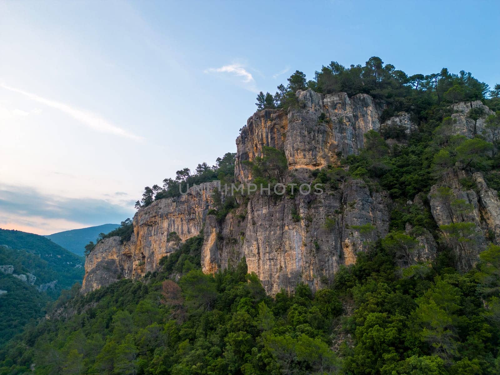 Steep rocky cliffs over forested landscape at golden hour. High quality photo