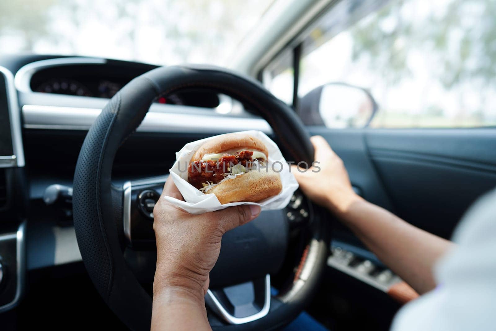 Asian woman driver hold and eat hamburger in car, dangerous and risk an accident.