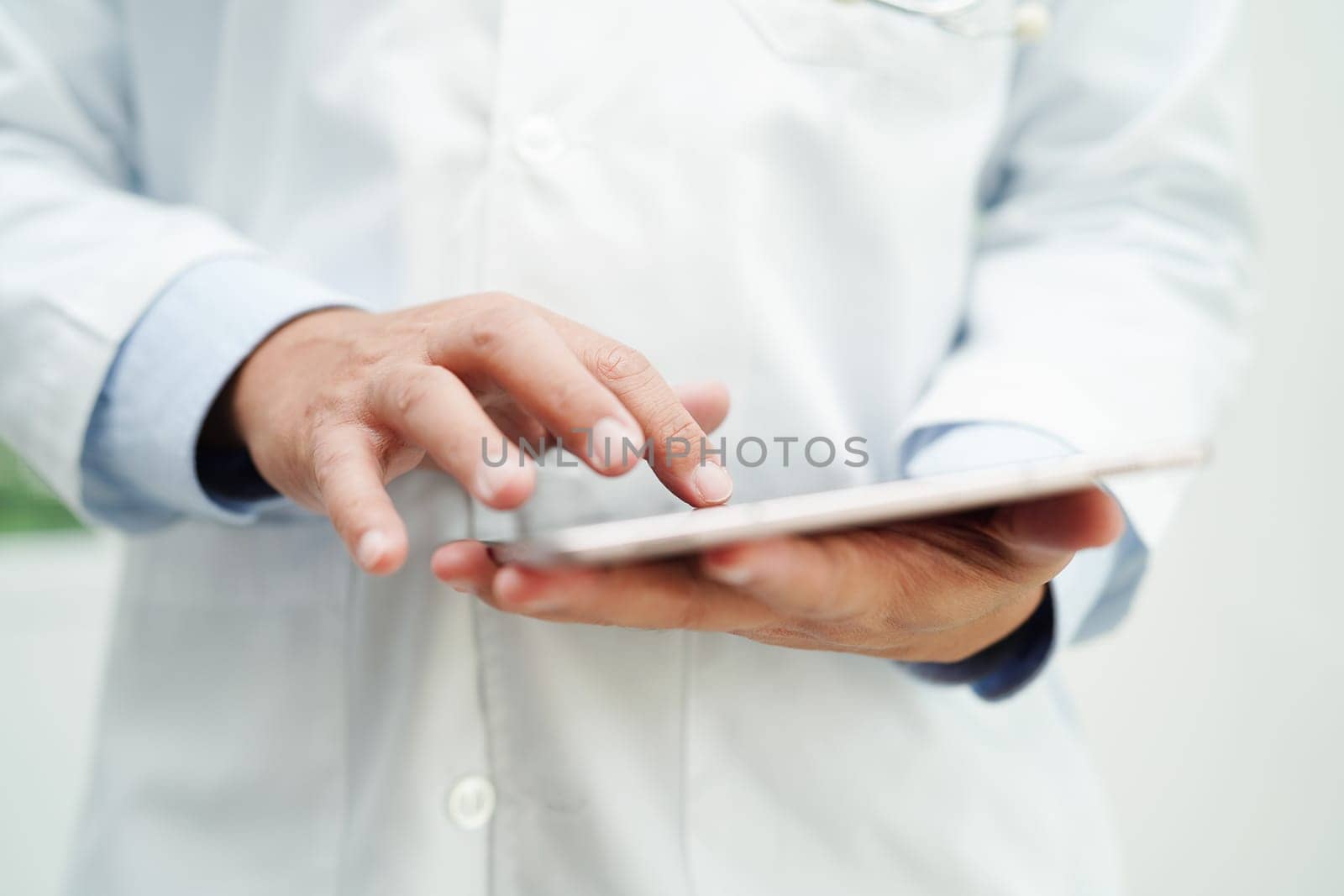 Asian man doctor using tablet computer to reading patient report, check up and search for solve treatment health medical online in hospital.