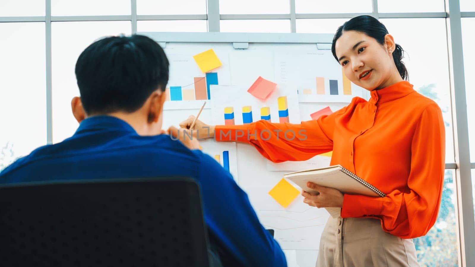 Young woman explains business data on white board in casual office room . The confident Asian businesswoman reports information progress of a business project to partner to determine strategy . Jivy