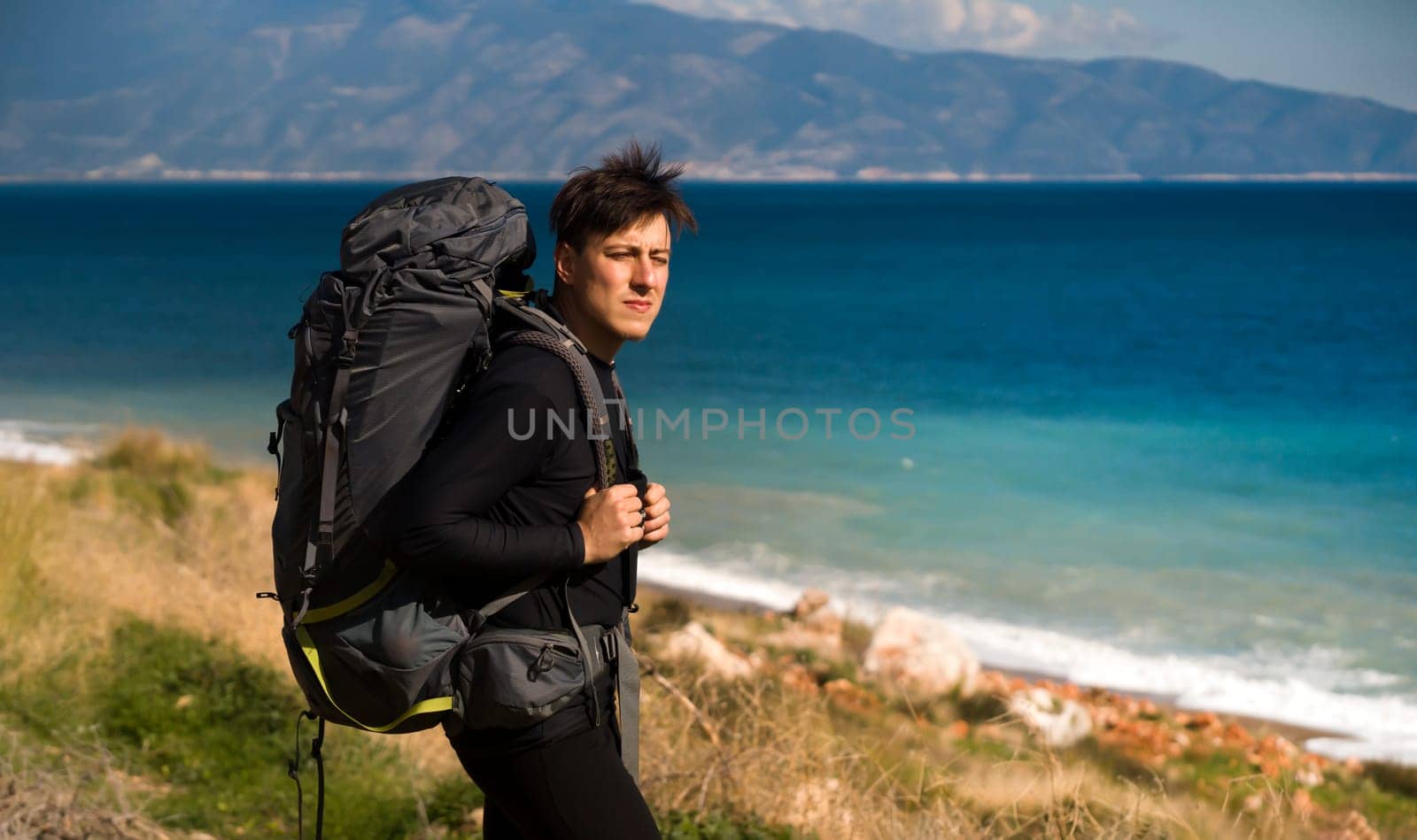A young man travels, tracks and walks along the sea coast on a sunny day with a backpack at sunset. A traveler enjoys the seascape during his vacation.