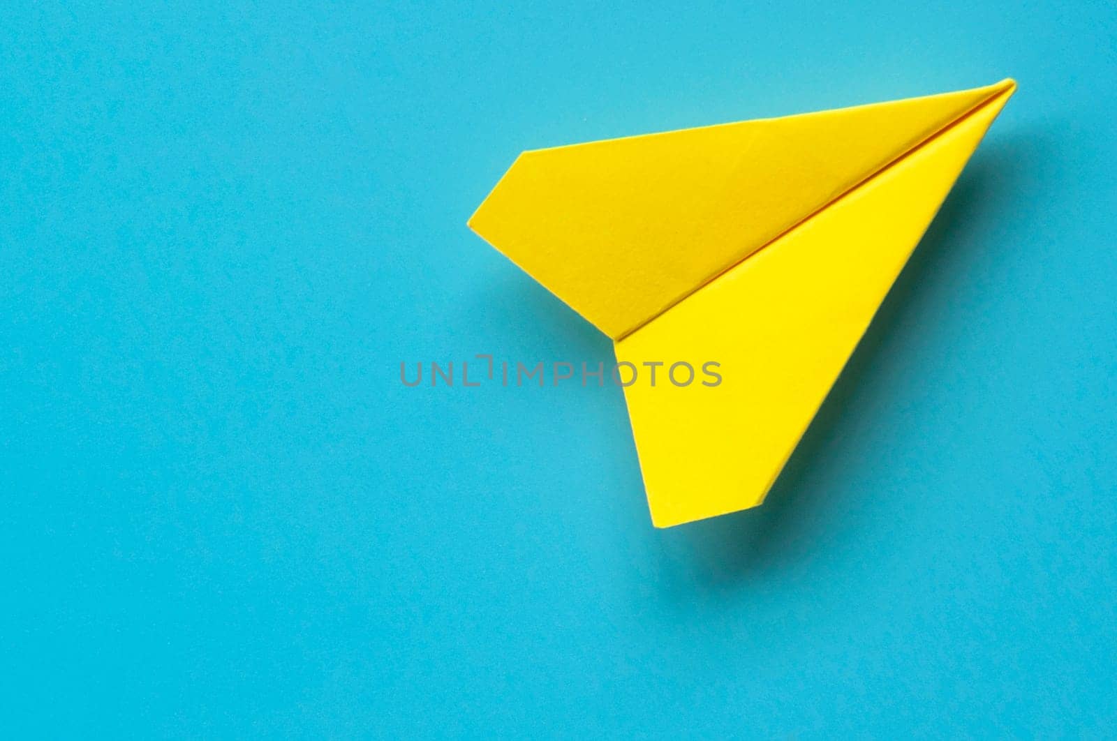 Top view of yellow paper airplane on blue background with customizable space for text.