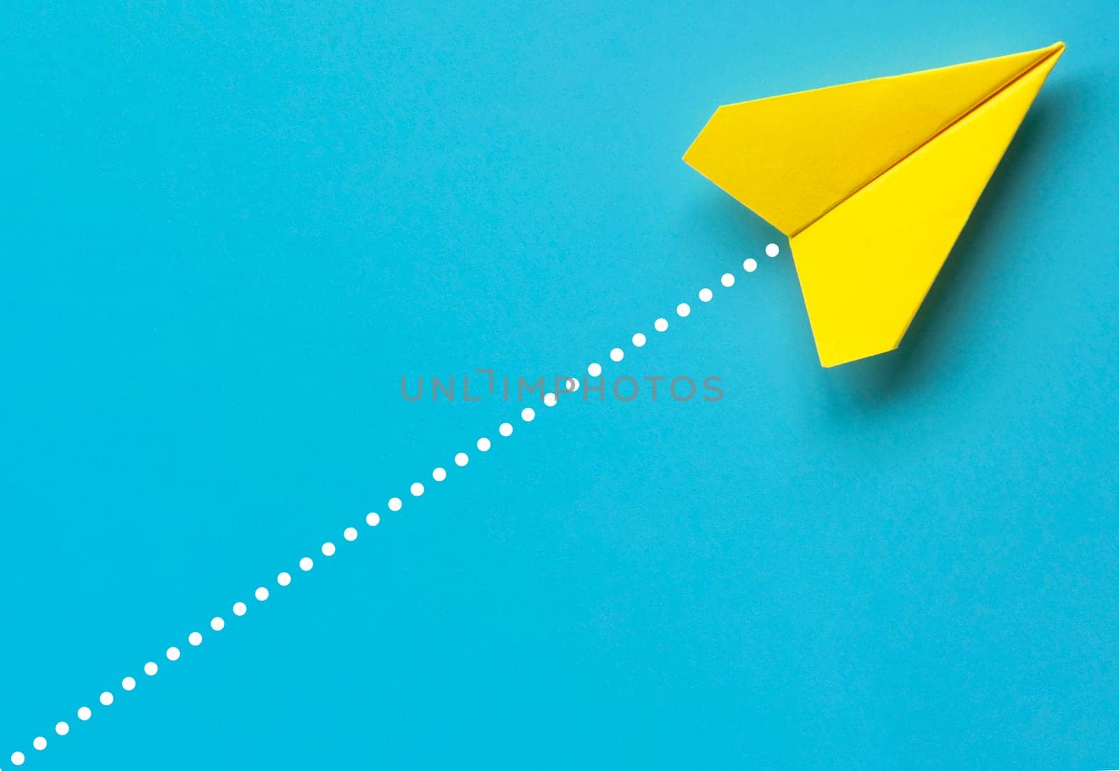 Top view of yellow paper airplane on blue background.