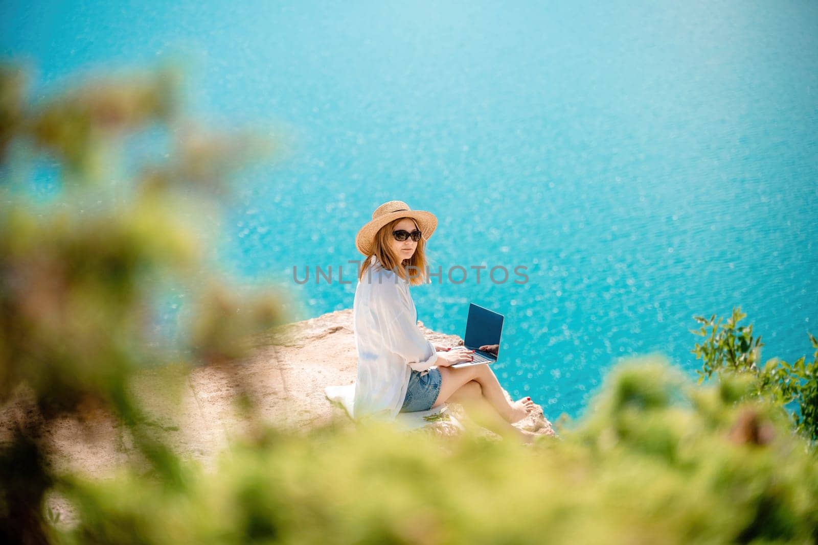 Freelance woman working on a laptop by the sea, typing away on the keyboard while enjoying the beautiful view, highlighting the idea of remote work