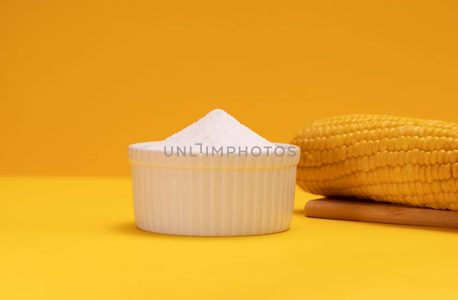 Erythritol, organic sweetener produced by fermentation from corn, called dextrose in ceramic bowl on yellow orange background, bunch of corn. Sugar substitute. Horizontal plane, copy space for text.