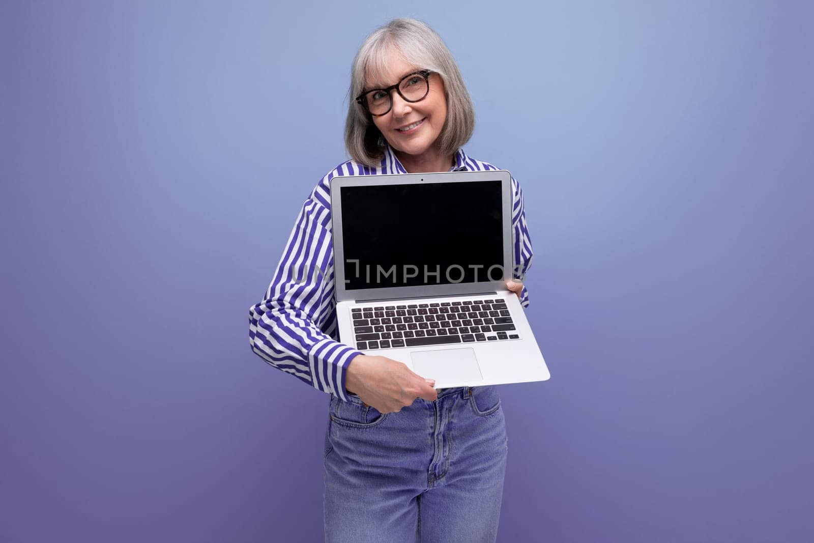 smiling 60s mature woman with gray hair with laptop mockup on bright studio background.