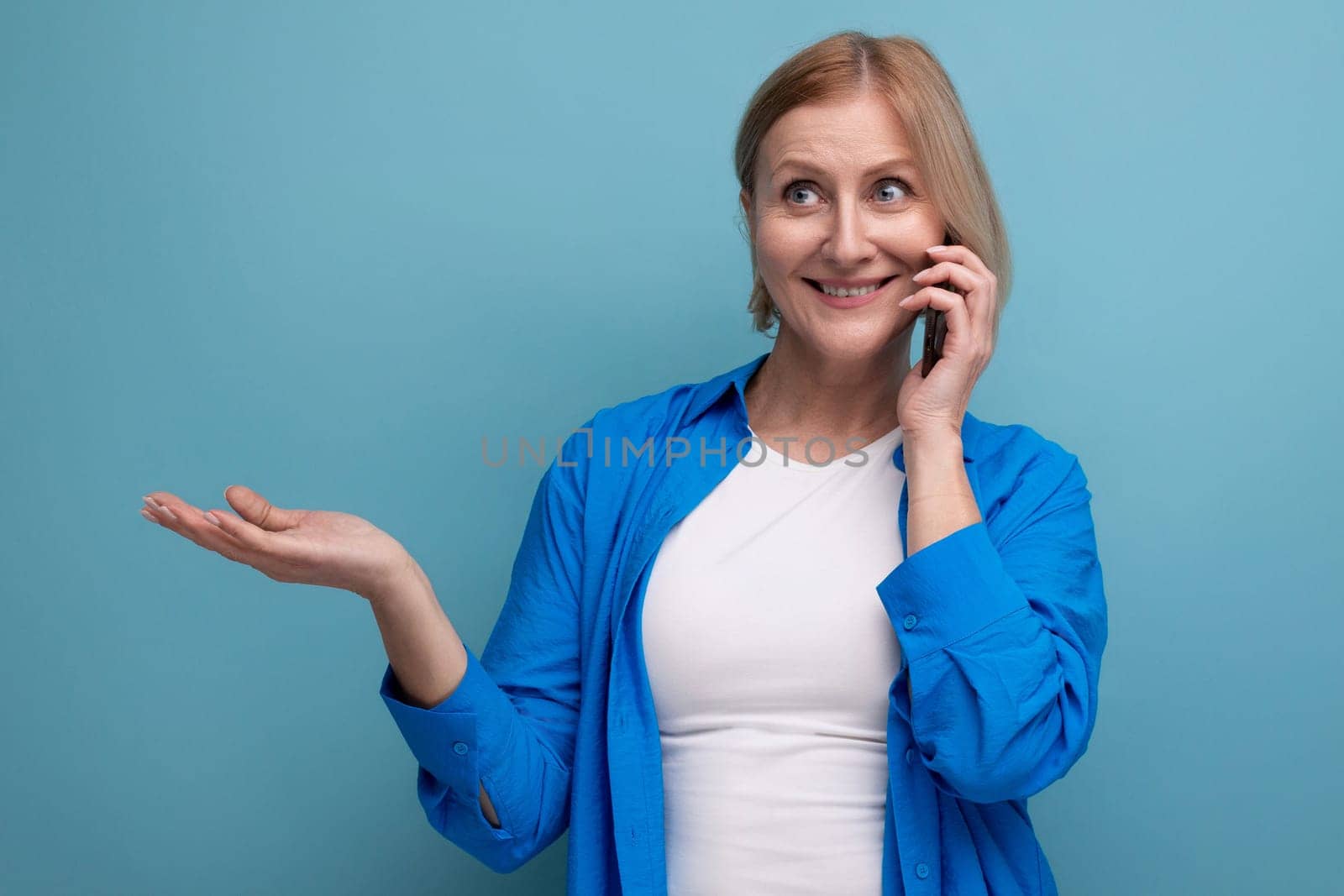 middle aged woman chatting using smartphone on blue background copy space by TRMK