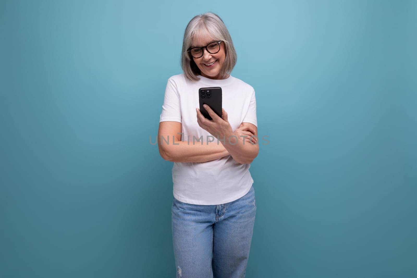 gray-haired mature woman studying digital technology smartphone on a bright studio background.