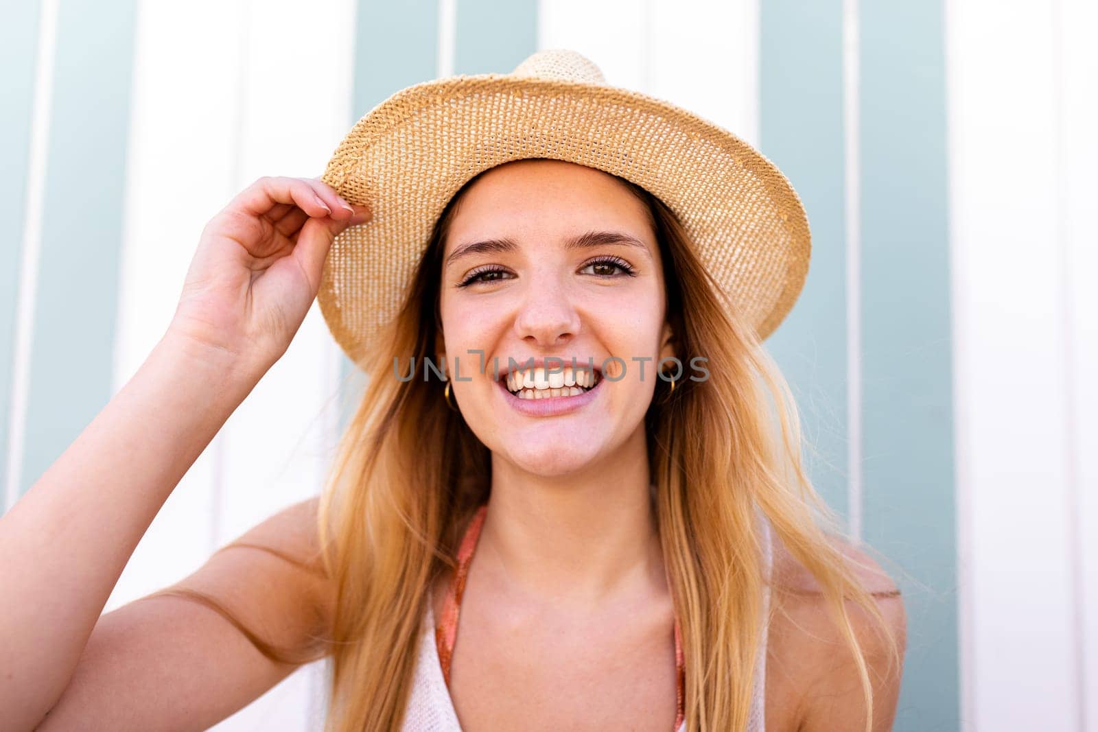 Headshot of young happy blond woman wearing summer hat looking at camera. by Hoverstock