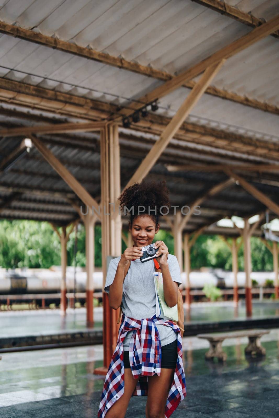 Asian teenage girl african american traveling using a camera take a photo to capture memories while waiting for a train at the station. by Manastrong