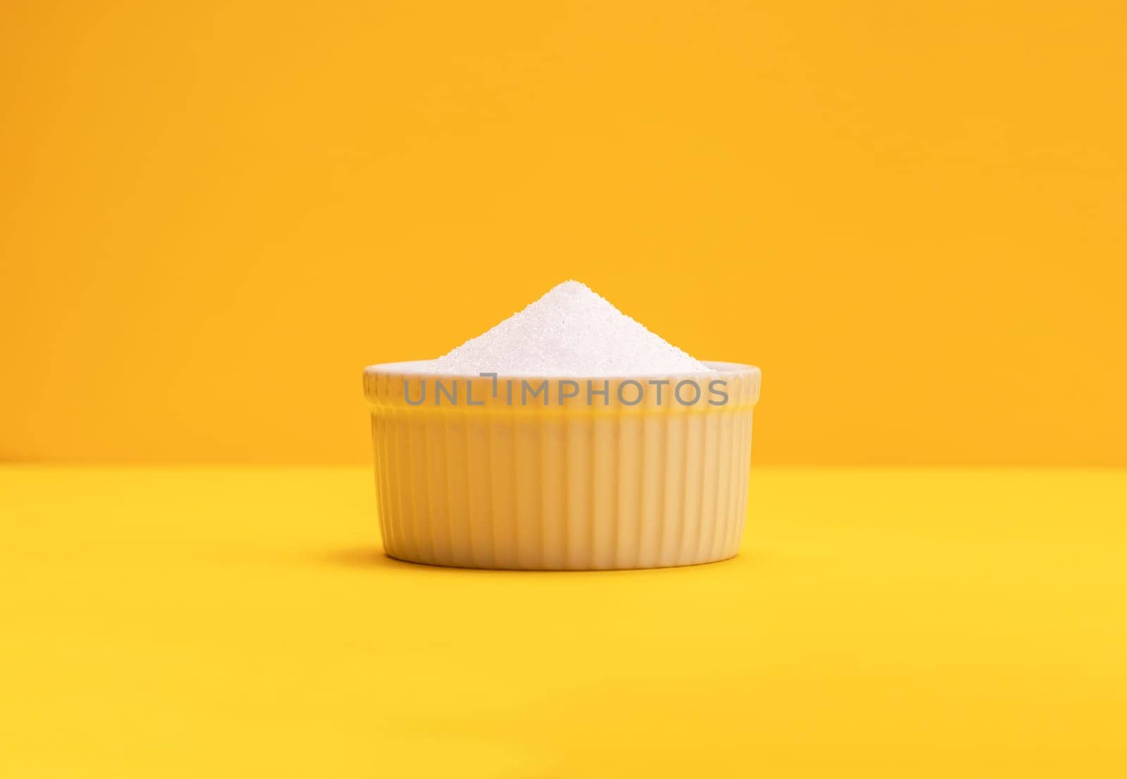 Natural organic sweetener Erythritol, produced by fermentation from corn, called dextrose in ceramic bowl on yellow orange background. Sugar substitute. Horizontal plane, copy space for text.