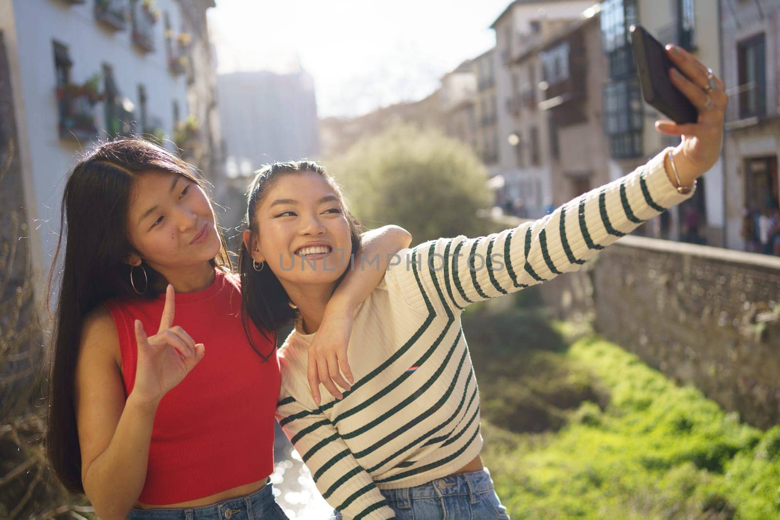 Young Asian female friends taking self portrait on cellphone during sightseeing by javiindy