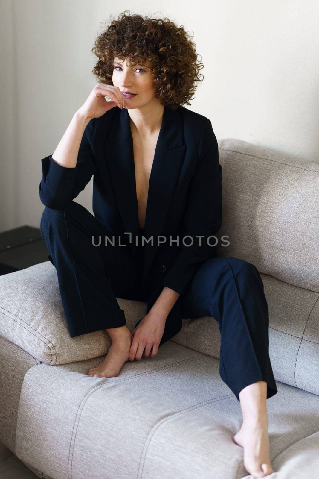 Woman in suit with bare chest sitting on sofa by javiindy