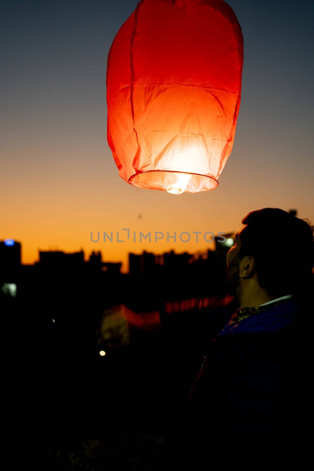 silhouette of man pushing up paper sky lantern with flame at bottom at sunset on sankranti uttarayan, independence day by Shalinimathur