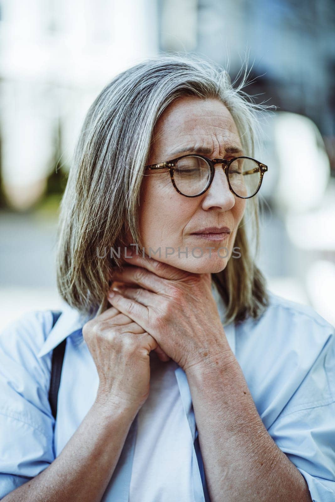 Concept of sickness through mature lady holding throat. Woman appears sick and tired, with weary expression on face. Cold toned color palette, adding to overall sense of illness and discomfort. . High quality photo