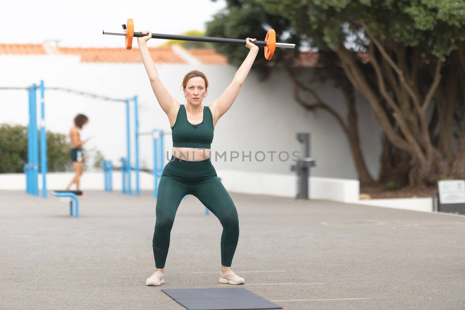 Adult sportive woman lifting a dumbbell on the outdoors sports ground. Mid shot