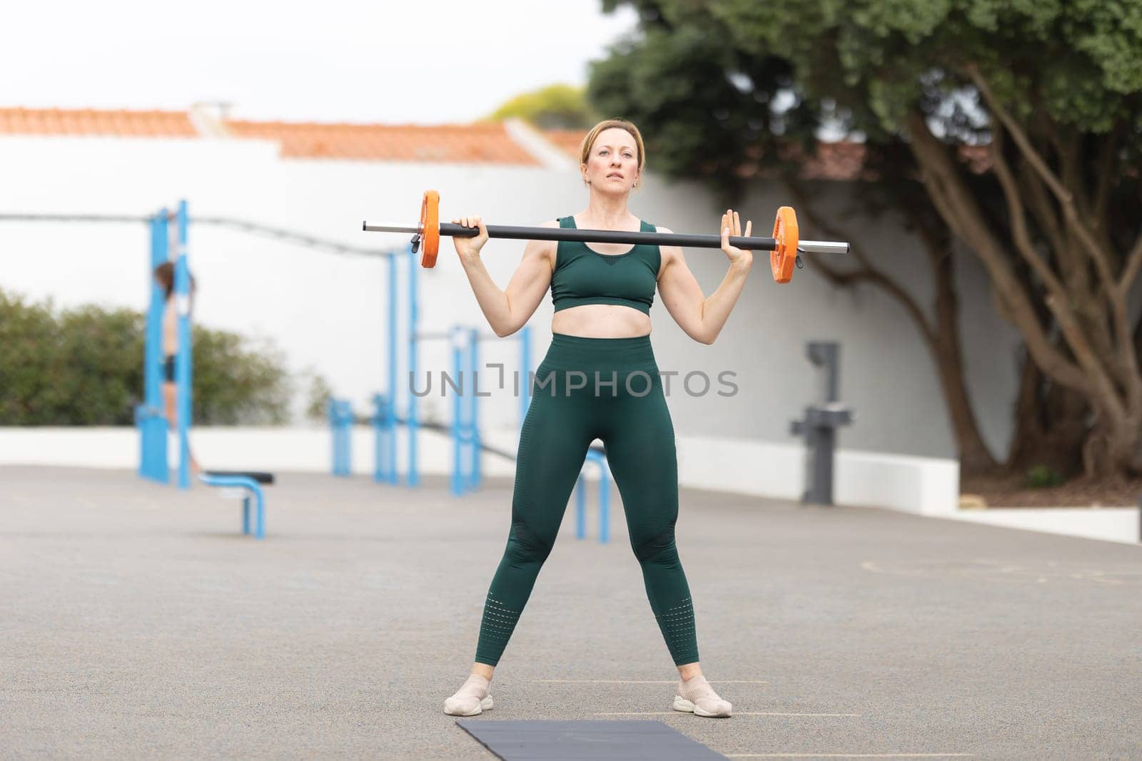 Adult sportive woman lifting a dumbbell on the sports ground. Mid shot