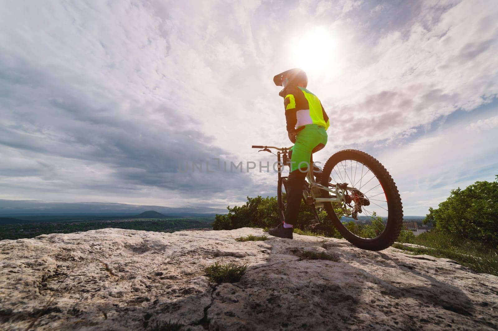 A young man in sportswear stands near a mountain bike and looks to the side while choosing a trajectory for a competition. Athlete resting from training.