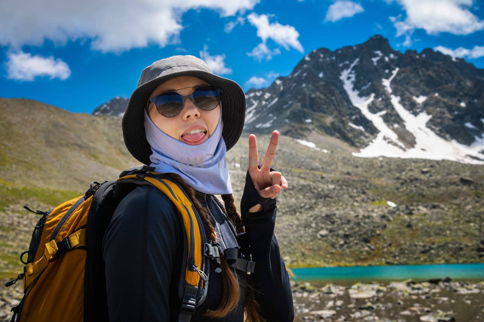 hipster shows tongue, funny face, posing in the countryside on a sunny day, stylish hat and sunglasses. woman with a backpack on a hike rejoices.