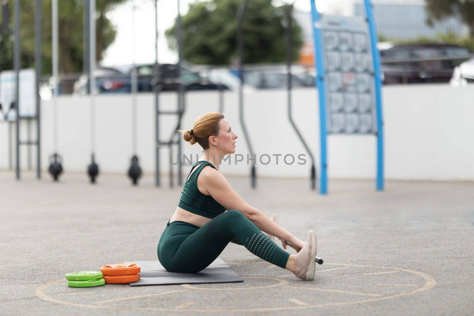 Adult athletic woman exercising with a barbell outdoors. Mid shot