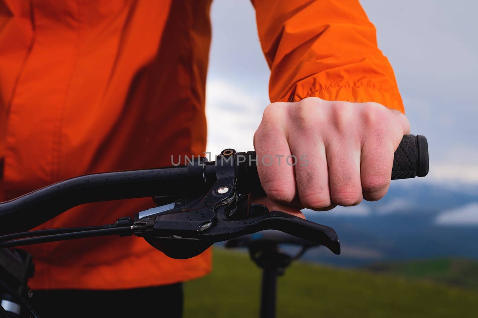 A male cyclist holds a handlebar of a mountain bike in a mountain protected park, close-up image, face is not visible, unrecognizable person.