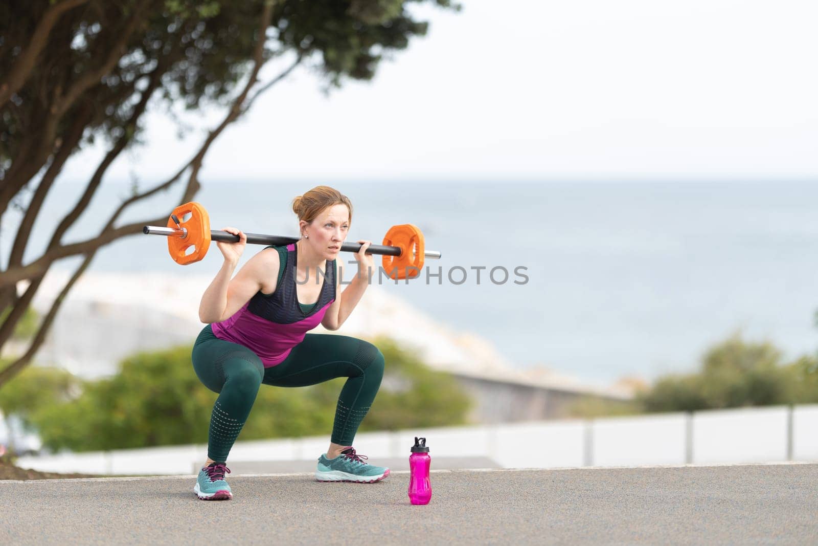 Adult athletic woman squatting with a dumbbell on her shoulders. Mid shot