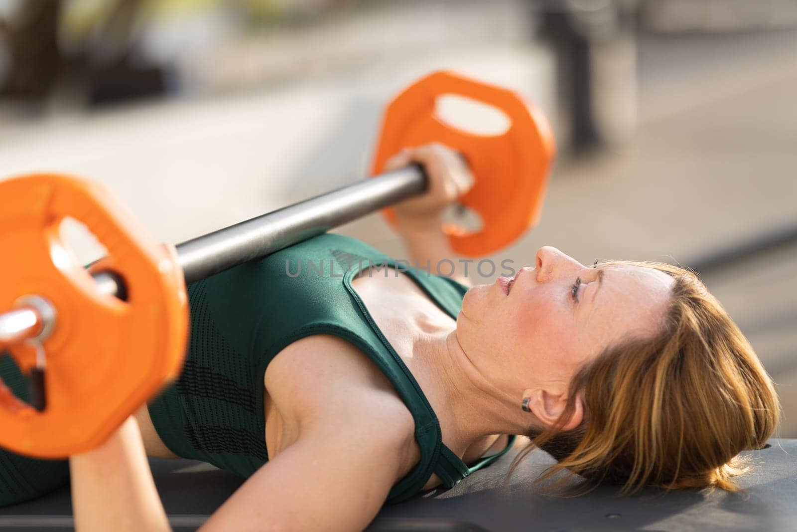 Adult fitness woman training her hands with lifting dumbbell lying down on yoga mat. Mid shot