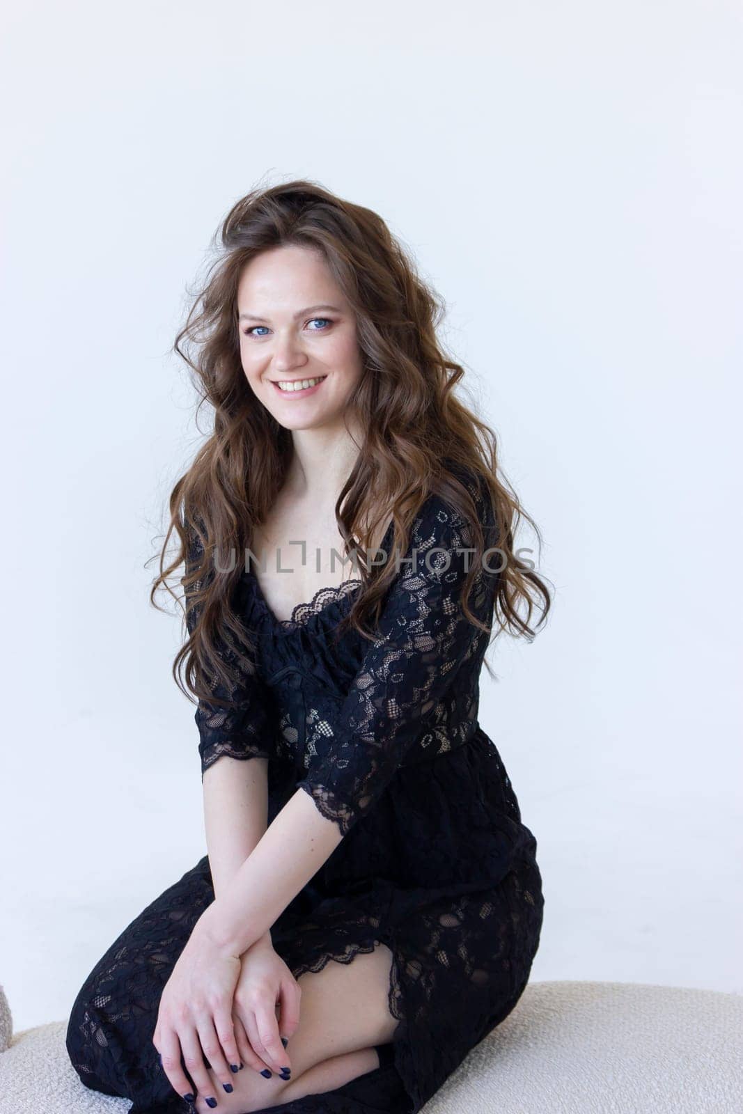 Portrait Happy Smiling Young Woman Sits On Beige Lounge Couch, Sofa Looking At Camera On White Background. Beautiful Caucasian Female With Long Brown Hair. Modern Furniture. Vertical Plane.