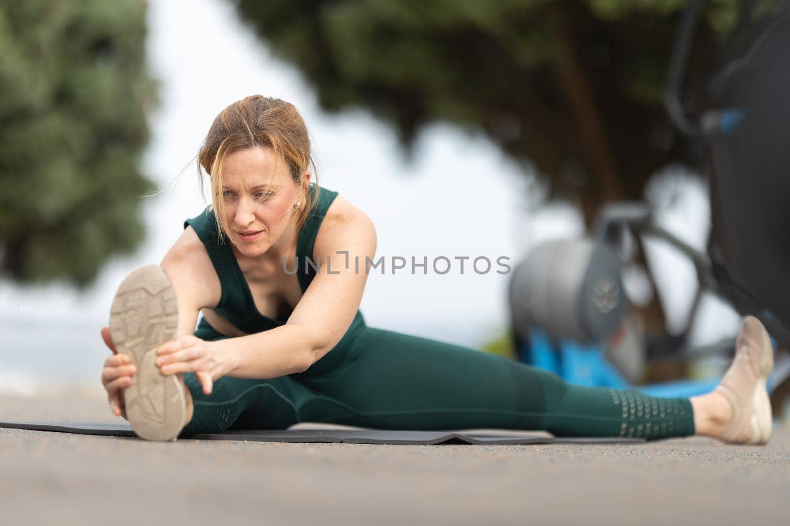 Adult sportive woman sitting in a splits at the outdoor sports ground and stretching to the side. Mid shot
