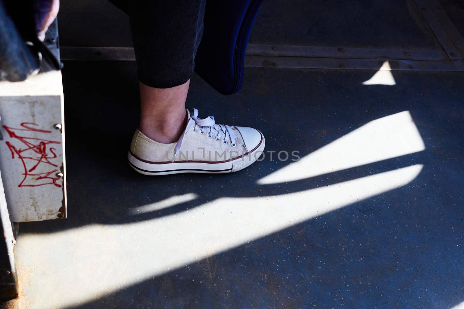 Photo of white sneakers on woman's leg against background of floor covering. Shoes.