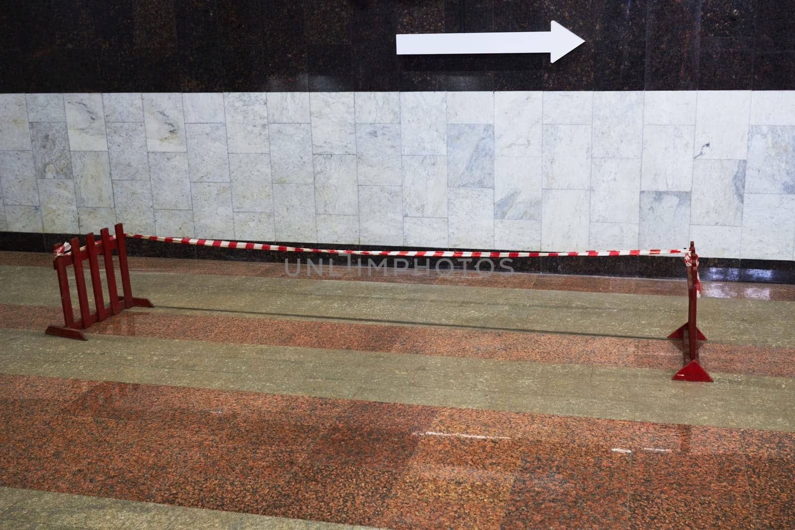 Photo of arrow to right against background of marble wall in subway. Wooden fences. Prohibition of passage. Damaged floor covering.