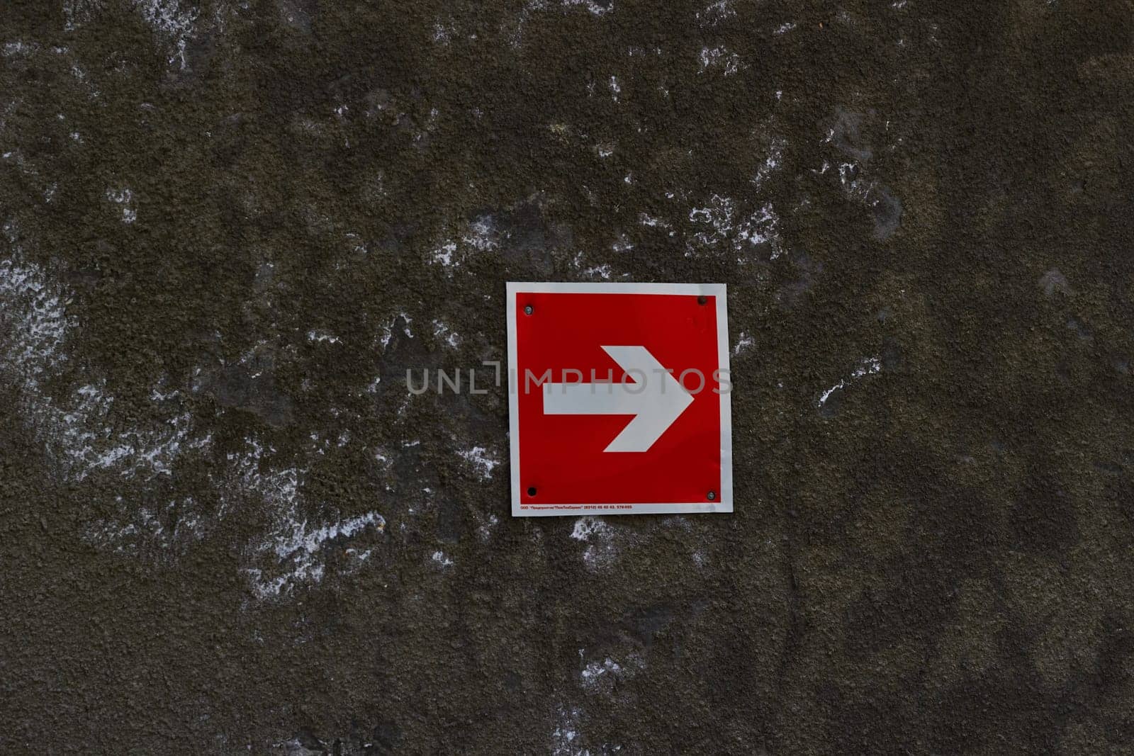 Photo sign of white arrow in red square against gray concrete wall. Right turn . Abstract background. Traffic Laws.
