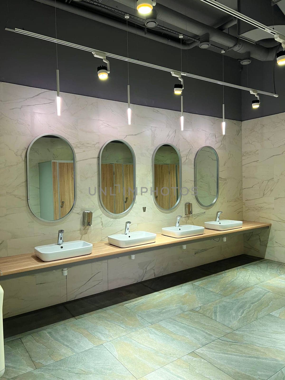 Modern restroom interior with stone gray tiles. Contemporary interior of public toilet. minimal interior with white tiles, round mirrors. Perspective of men's restroom. commercial bathroom.