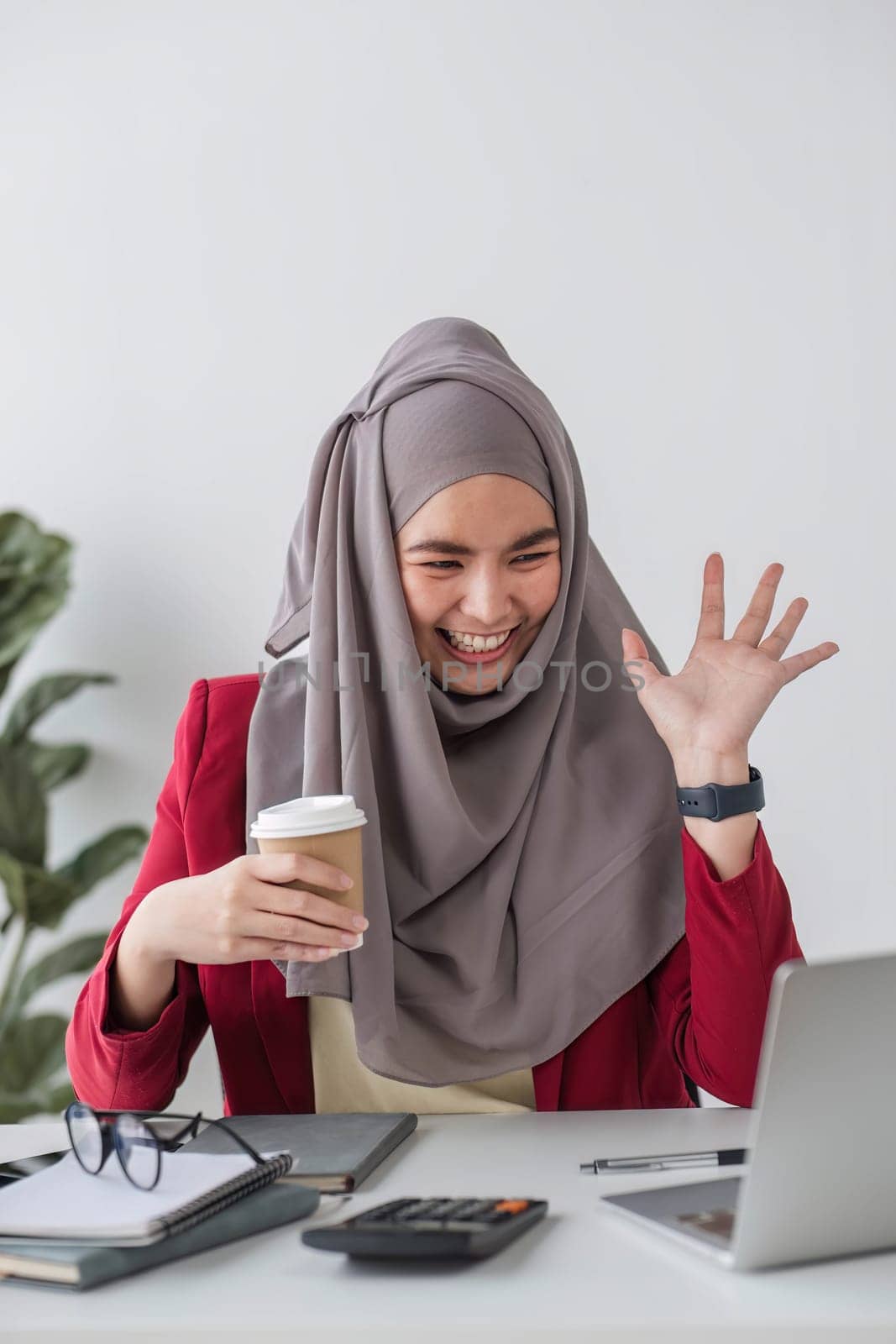 Portrait of beautiful muslim businesswoman smiling at the camera, sitting at her desk. by wichayada