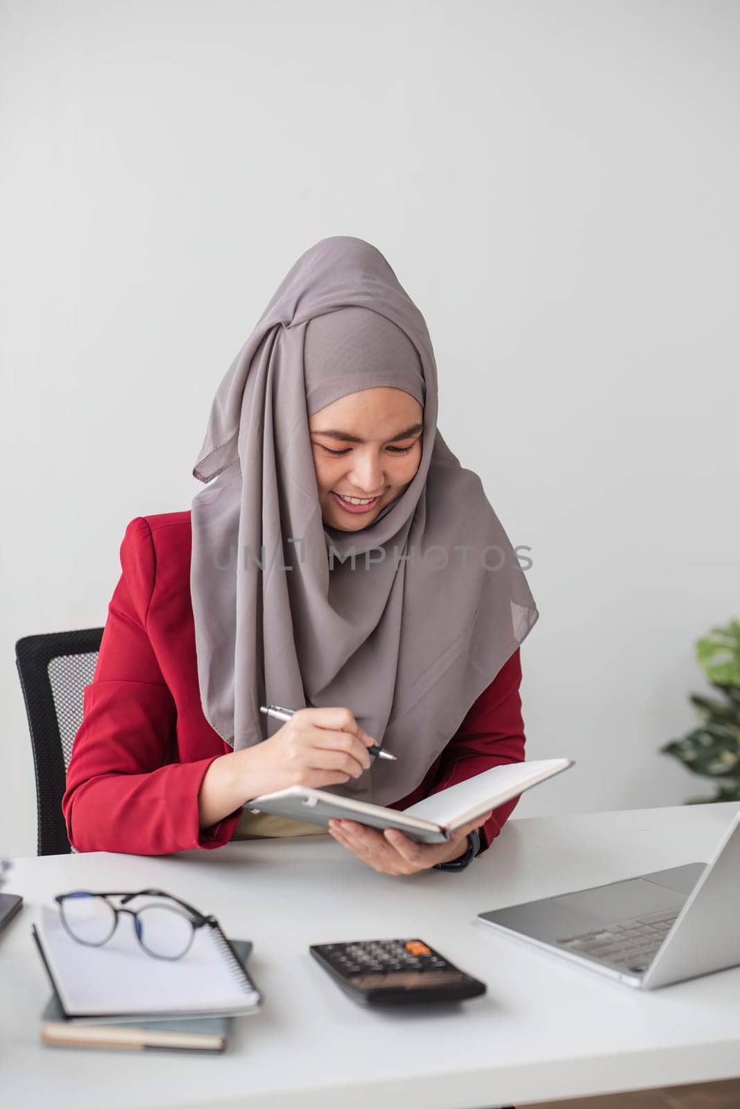 Portrait of beautiful muslim businesswoman smiling at the camera, sitting at her desk. by wichayada