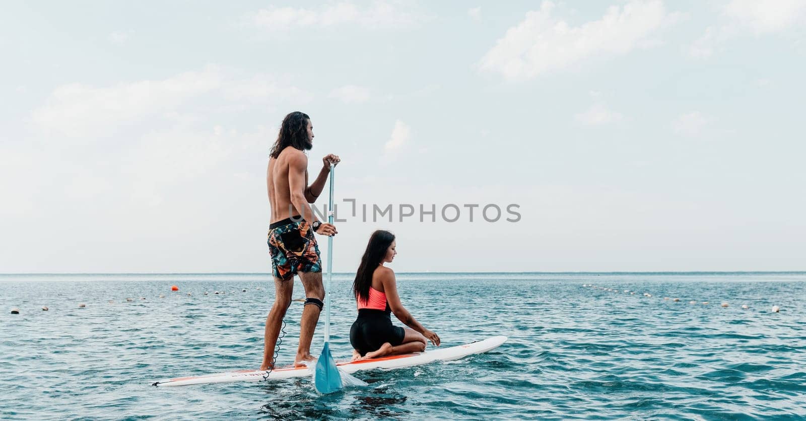 Sea woman and man on sup. Silhouette of happy young woman and man, surfing on SUP board, confident paddling through water surface. Idyllic sunset. Active lifestyle at sea or river