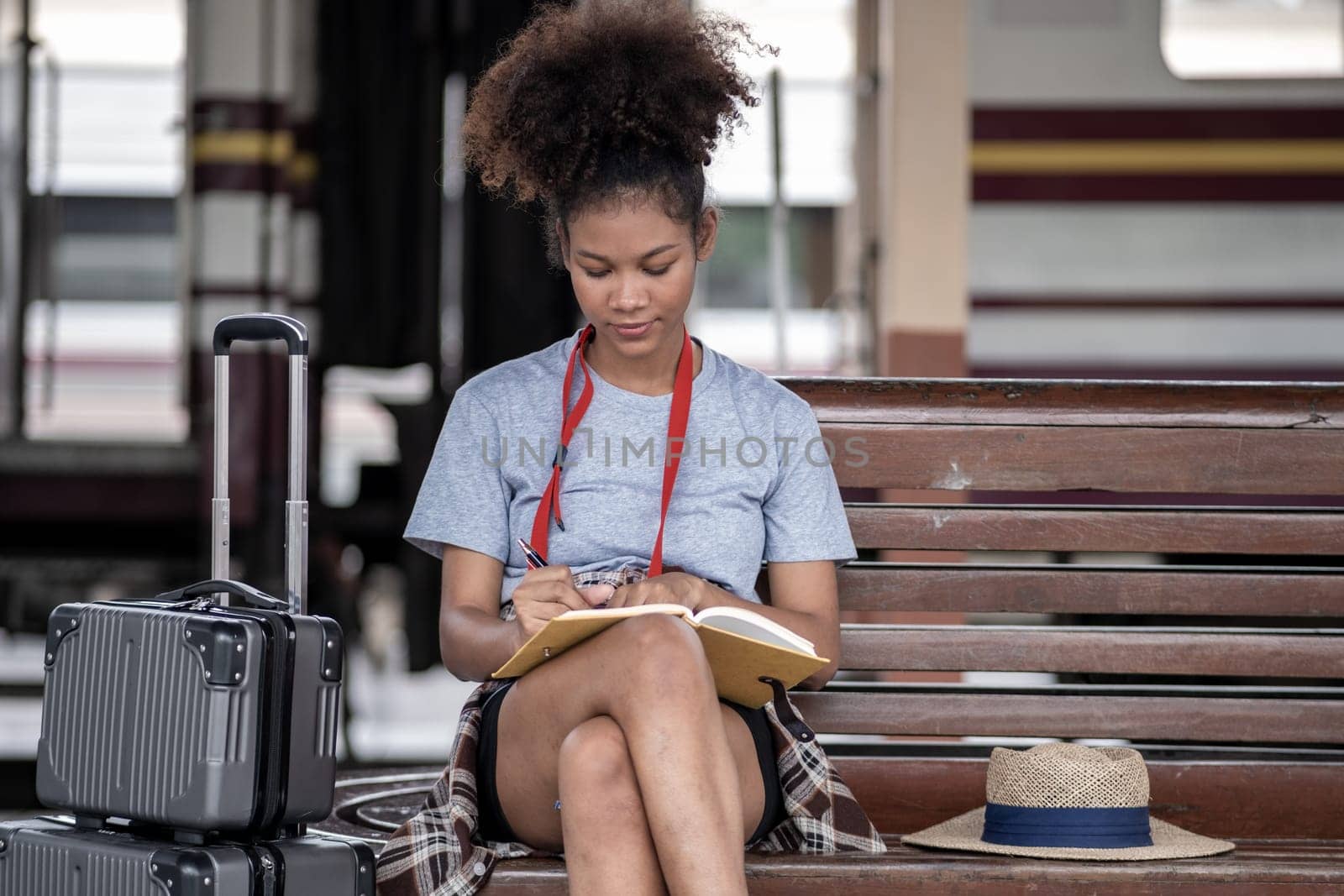 Asian African female tourist traveler holding mobile phone smart phone sitting at train station, Confident smiling teenager girl playing smart phone laptop computer on suit case at station. High quality photo