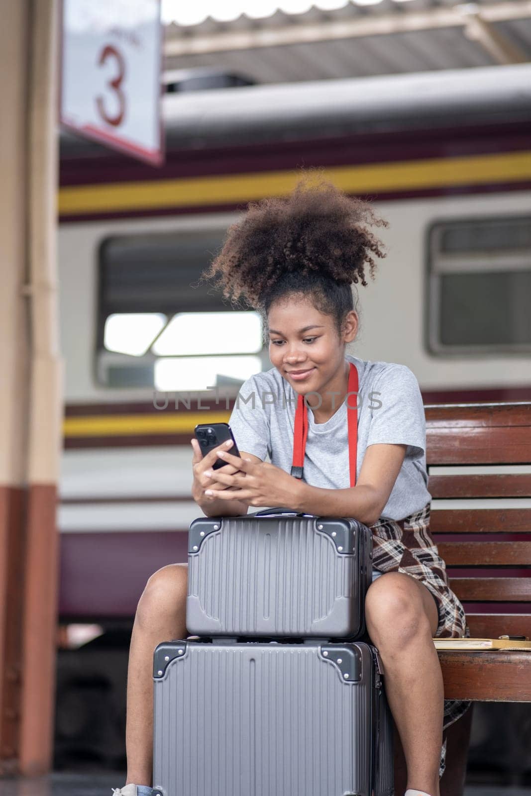 Asian African female tourist traveler holding mobile phone smart phone sitting at train station, Confident smiling by wuttichaicci