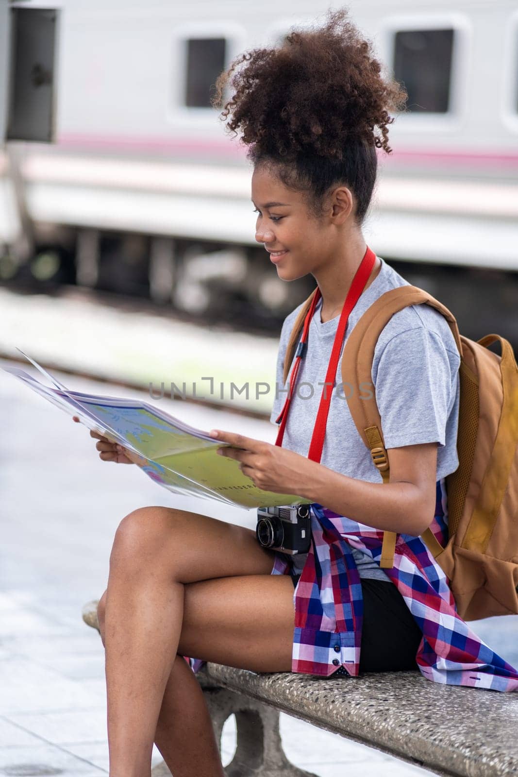 Young woman female smiling traveler with back pack looking to map while waiting for the train at train station by wuttichaicci