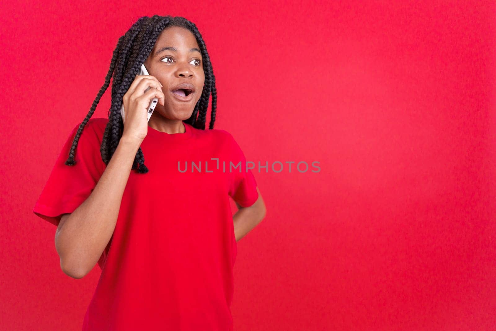 Surprised african woman talking to the mobile in studio with red background