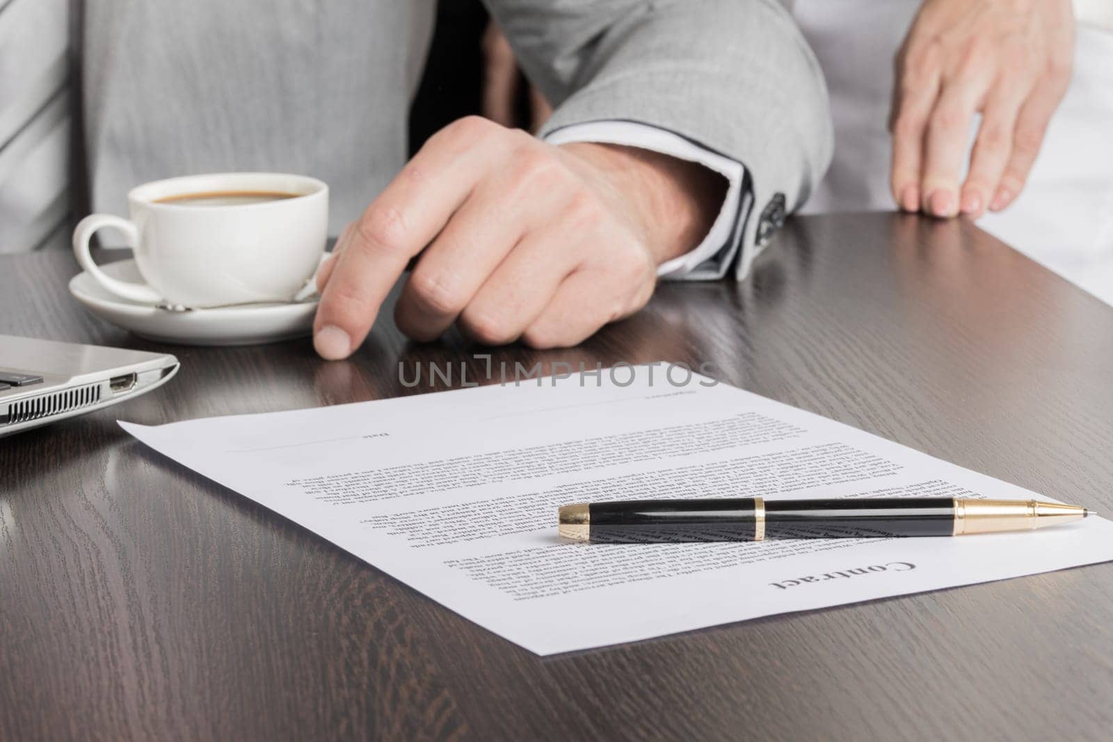 Close up photo of businessman sitting at office desk in front of laptop and working with contract document