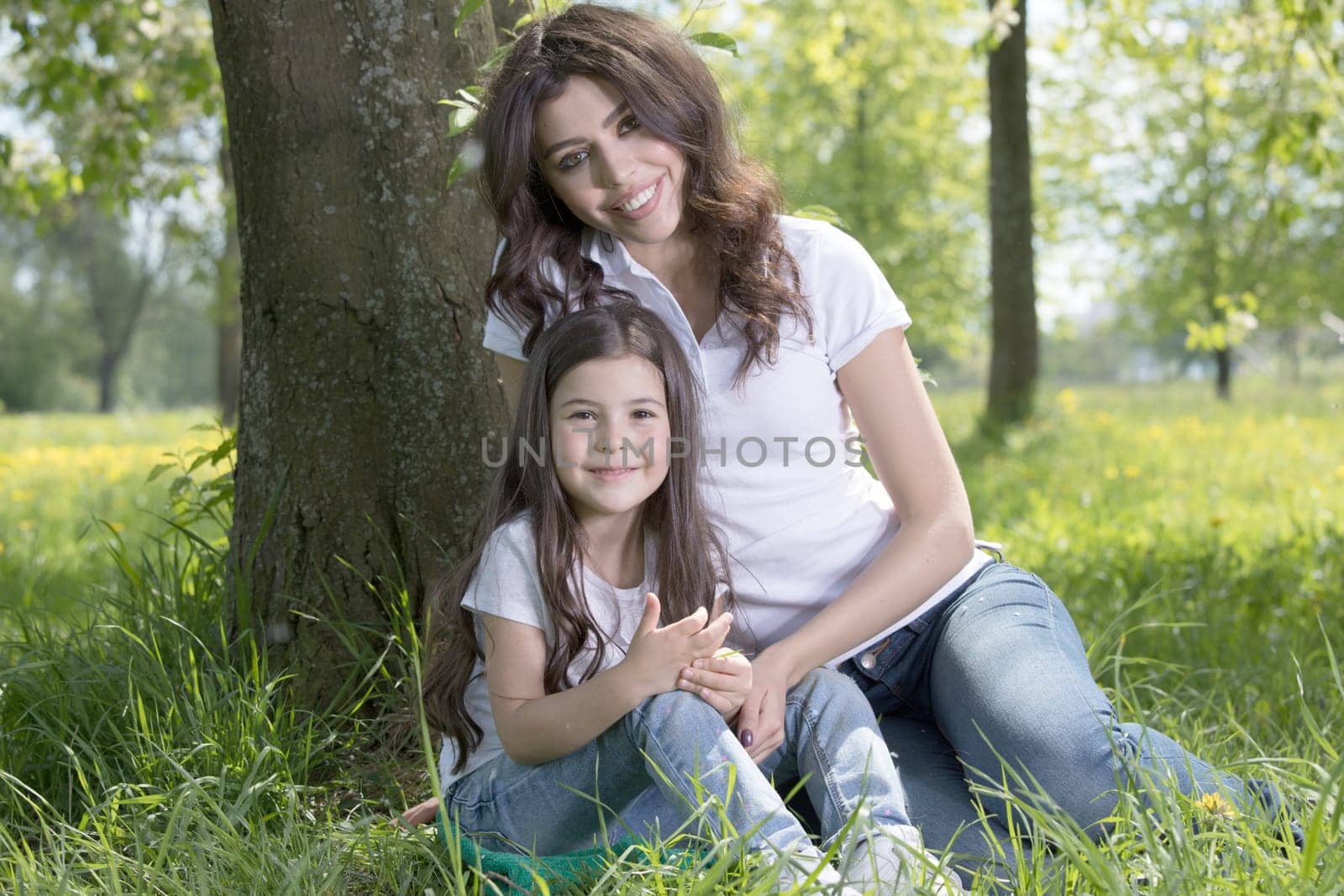 Beautiful young mother and daughter relaxing sitting on grass in park