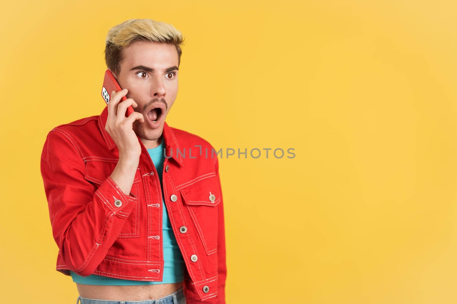 Surprised gay man talking to the mobile phone in studio with yellow background