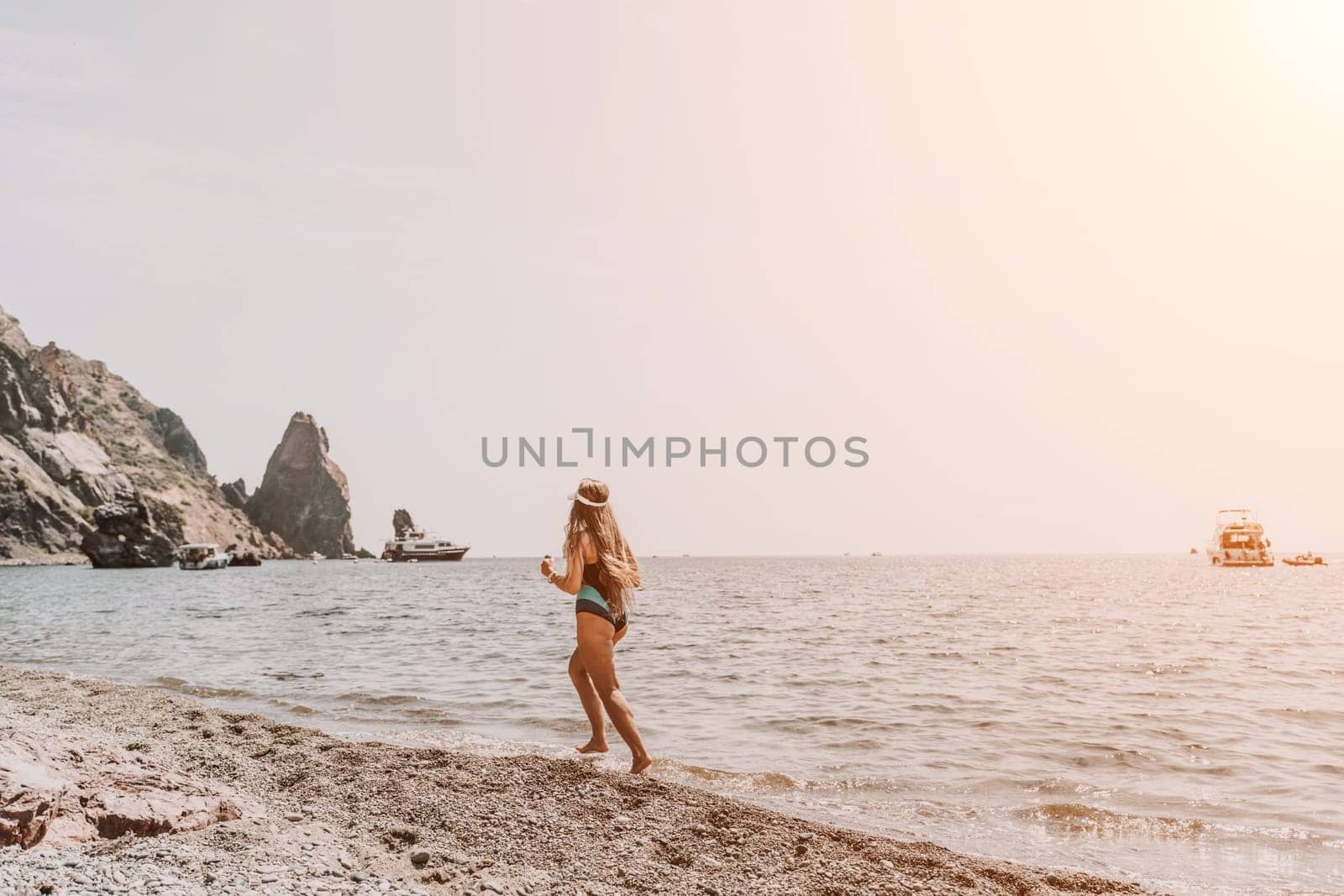 Woman travel summer sea. A happy tourist in a blue bikini enjoying the scenic view of the sea and volcanic mountains while taking pictures to capture the memories of her travel adventure